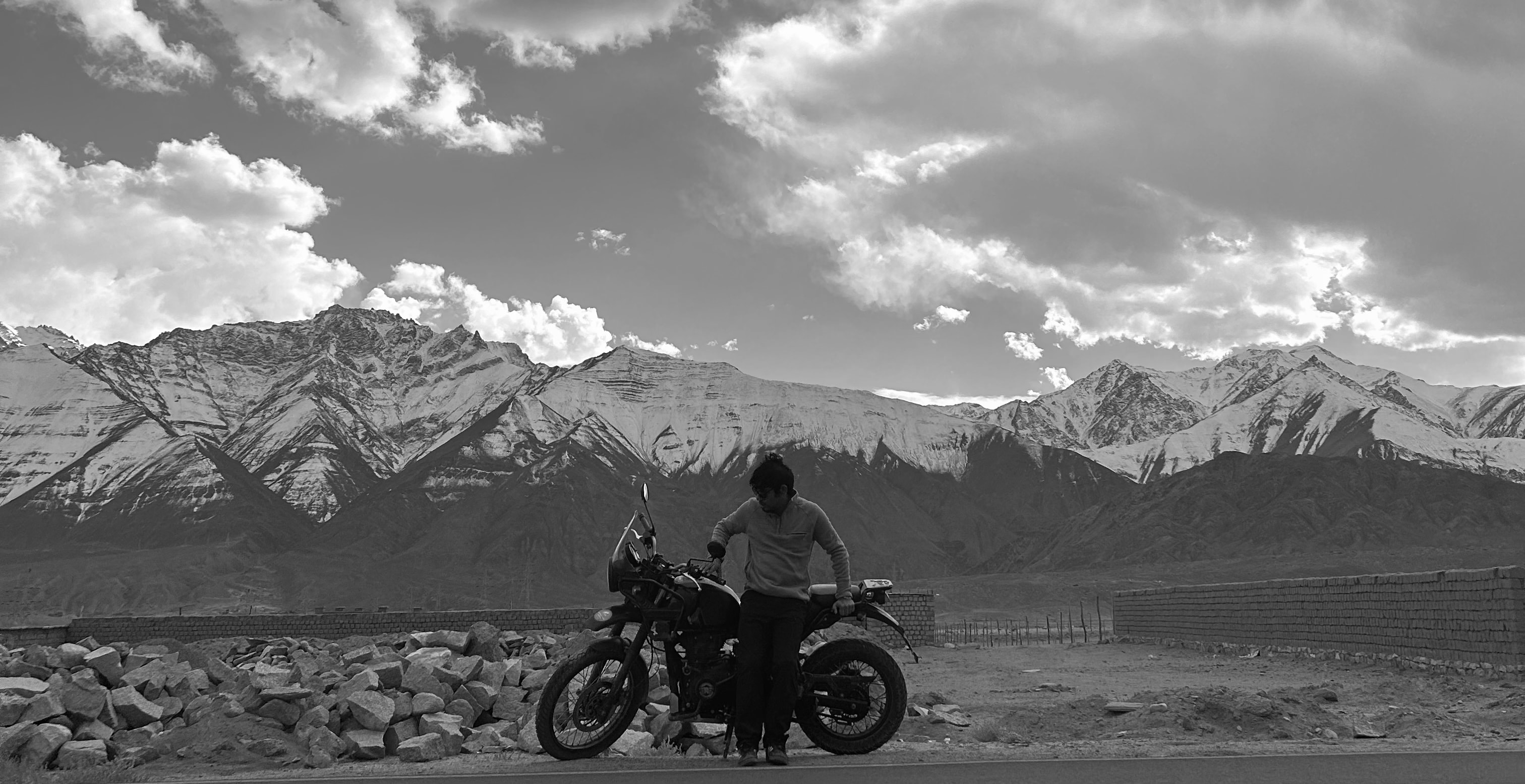 Standing beside a motorcycle on a road below a snow-capped range